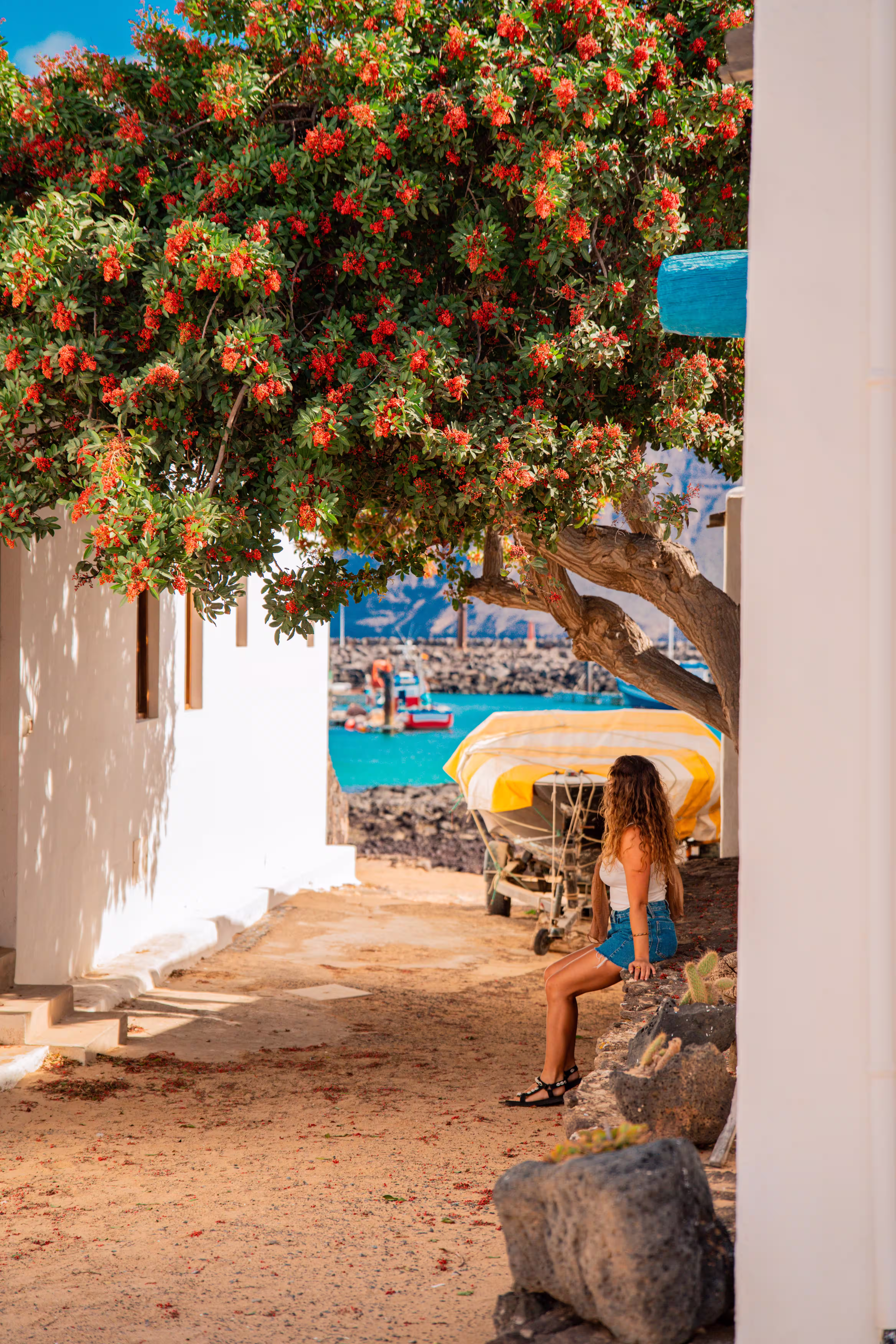 Donna seduta sotto un albero in una strada di sabbia a La Graciosa